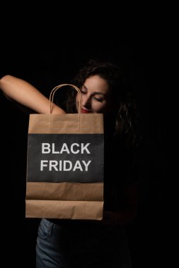 Kara Cuma alışveriş çantasını kucaklayan mutlu müşteri, indirimlerin ve satışların keyfini çıkarıyor.