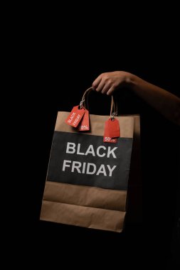 Müşteri elinde siyah cuma reklamları ve indirim etiketleriyle alışveriş çantası tutuyor, mevsimlik satışları ve alışveriş anlaşmalarını destekliyor