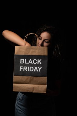 Siyah bir arka planda siyah bir Cuma alışveriş çantası tutan kadın.