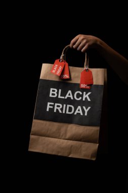 Kara Cuma logosu olan alışveriş çantası ve siyah arka planda tutulan indirim etiketleri.