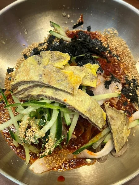 Naengmyeon, üzerine dilimlenmiş sebze, haşlanmış yumurta ve baharatlı sos serpilmiş soğuk Kore erişte tabağı. Yaz yemeği fotoğrafçılığı ve Kore mutfağı projeleri için mükemmel..