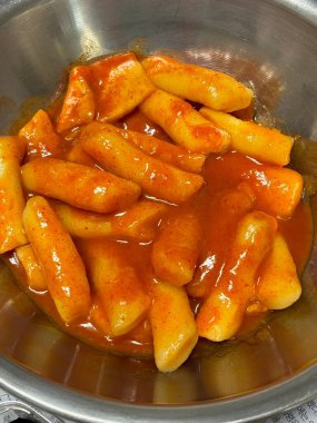 Çiğnenmiş kırmızı soslu pirinç kekleri ve susam tohumları ve yeşil soğanla kaplı baharatlı Kore tteokbokki. Bağımlılık yaratan tadı ve tatmin edici dokusuyla bilinen popüler bir sokak yemeği..