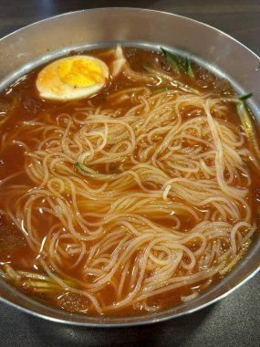 Naengmyeon, üzerine dilimlenmiş sebze, haşlanmış yumurta ve baharatlı sos serpilmiş soğuk Kore erişte tabağı. Yaz yemeği fotoğrafçılığı ve Kore mutfağı projeleri için mükemmel..