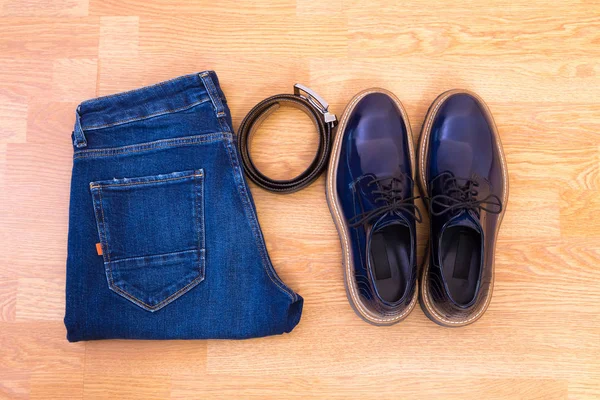 Men\'s jeans, leather belt and a pair of blue glossy shoes on wooden floor