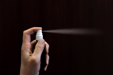 Koyu kahverengi arka planda antiseptik dezenfektan kullanan bir adam, yakın plan. Hijyen ve sağlık hizmetleri kavramı