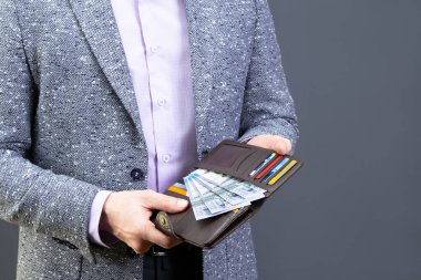 Gri ceketli bir adam, içinde Kazakistan banknotları ve kredi kartları olan kahverengi deri bir cüzdan taşıyor. Bankacılık ve finans kavramı