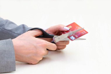Kırmızı kredi kartı modelini kesen bir kadın açık tahta arka planda makasla ellerini kapatıyor. Bankacılık ve finans kavramı