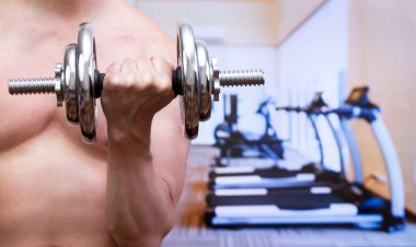 Metal bir dambıl tutan, arka planda bulanık spor salonu olan bir adam. Spor ve spor konsepti