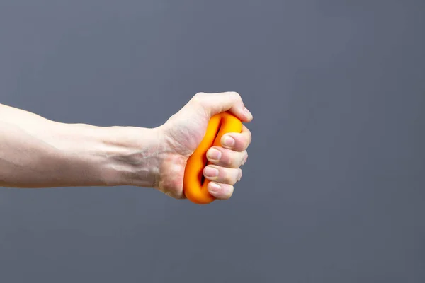 男子挤压橙色橡胶握力操纵器孤立在灰色背景 手部特写 体育和健身概念 — 图库照片