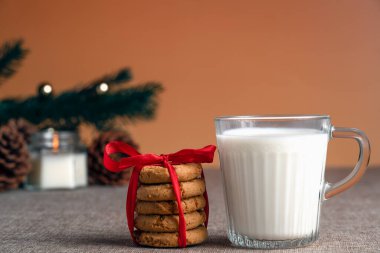 Kırsal bir zeminde kırmızı kurdeleyle bağlanmış bir bardak sütün yanında bir yığın tatil kurabiyesi.