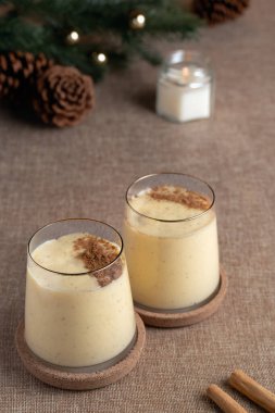 Yanında tarçın tozu ve tarçın çubuğu olan iki bardak klasik eggnog. Tatillerde eğlenmeye hazır.