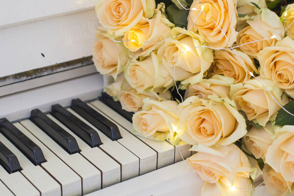 Персиковые розы с гирляндами на белом пианино
