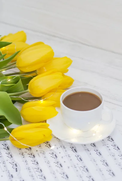 yellow tulips with garlands, a cup of coffee, cappuccino and notes on a white wooden background