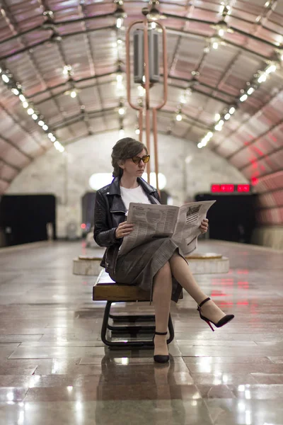 Business woman sitting reading a newspaper. Beautiful girl in a business suit and sunscreen sitting reading a newspaper at the subway station. A woman in a jacket. Success concept