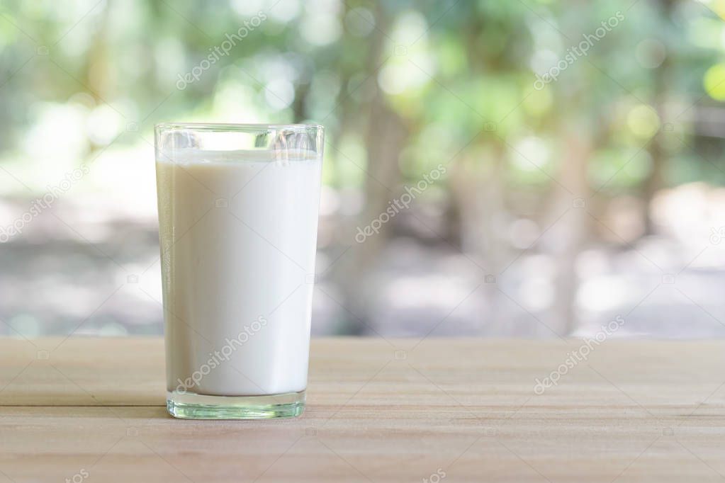 Glass of milk on desk with nature background.