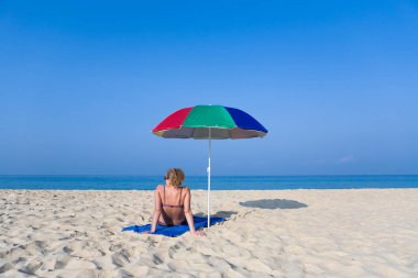 Yalnız bir kadın bir plaj şemsiyesi yanındaki sahilde oturuyor. Phuket.