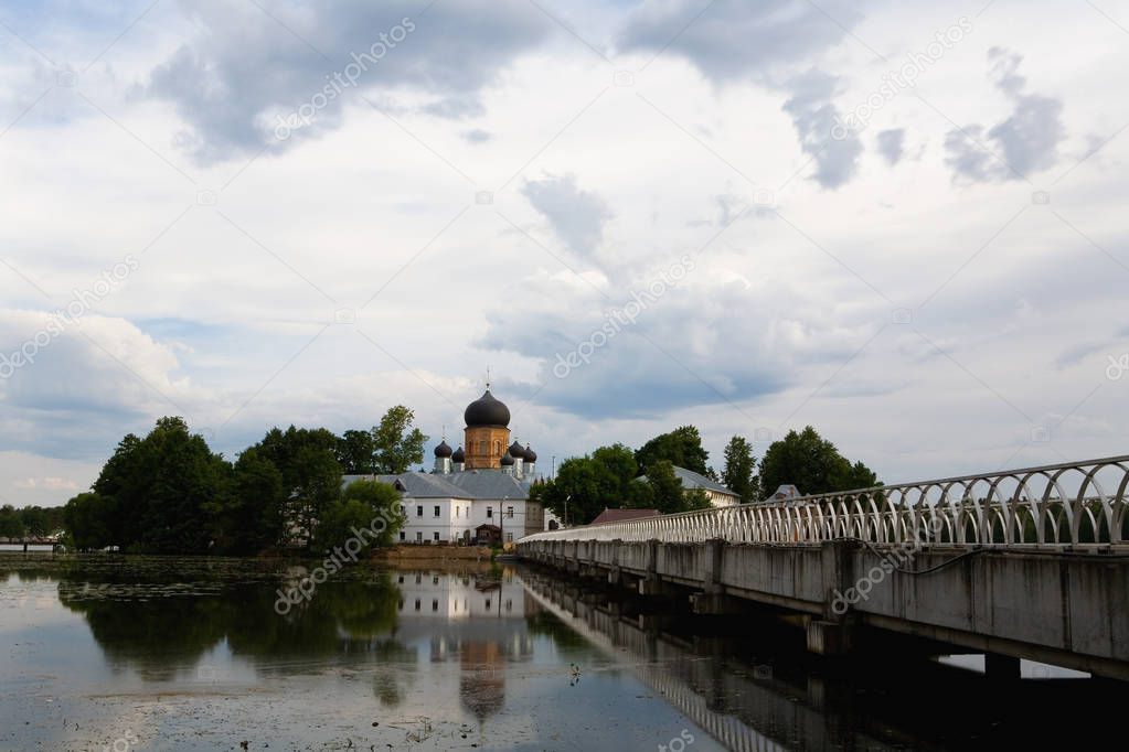 The bridge leads to the church on the shore of the pond. Russia.