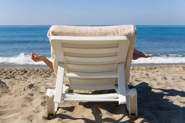 Bir kadın denizin kenarında şezlong üzerinde sigara içiyor. Beach tatil.