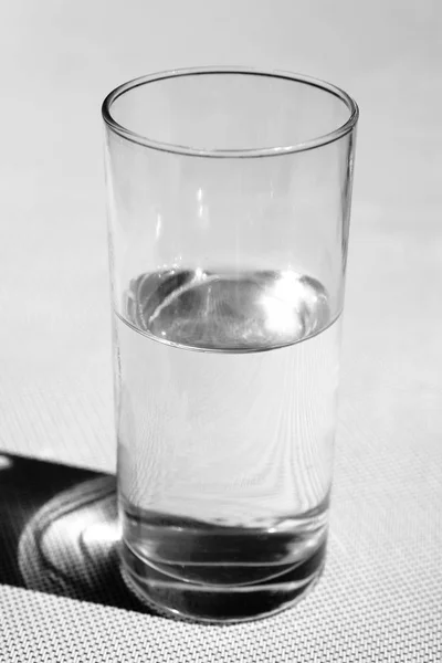 Sun glare reflected in a transparent glass of water. Black and white photo.