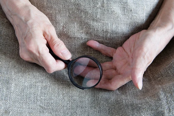 Hands of an old woman holding a magnifying glass. Close-up.