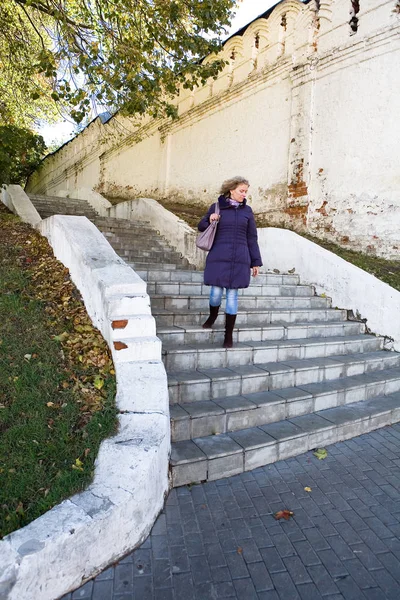 A beautiful young woman is walking down the stairs. Next to the wall of the Nativity of the Virgin monastery in the city of Vladimir