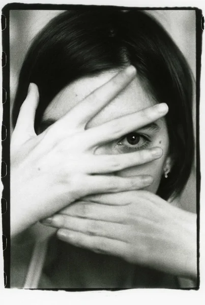 Kız elleriyle yüzünü gizler ve kameraya bakar.