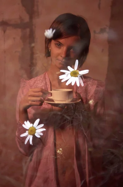 Flicka i en öppen mantel med en kopp i hennes händer och daisy blommor c — Stockfoto