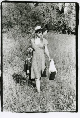 Şapkalı ve güneş gözlüklü bir kız plaj battaniyesiyle yürüyor. Dikkat! Görüntü, analog fotoğrafçılıktan kalan tahıl ve diğer eserler içeriyor.!