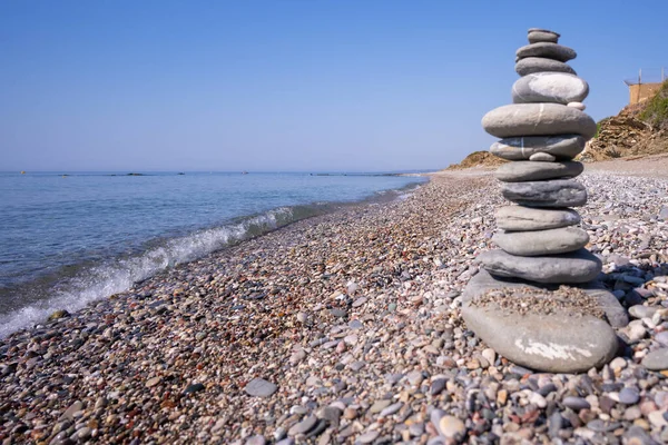 A balanced stack creative cairn made out of flat rocks erected with balance at the water's edge on a pebble sunny beach