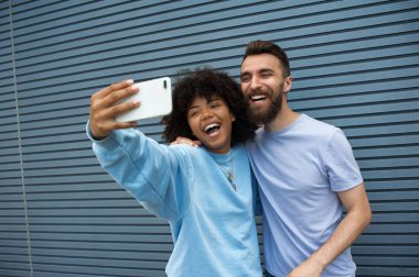Şirin hipster çift birbirlerine sarılma ve gündüz güzel bir günde bir kentsel inşaat zemin üzerine selfie çekerken gülümseyen gündelik kıyafeti giymiş.