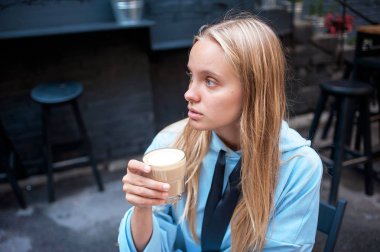 Hiç makyaj mavi kazak ve cappucino bardak café'de gündüz elinde uzun saç elbise ile güzel genç beyaz kız portresi yan görünümü.