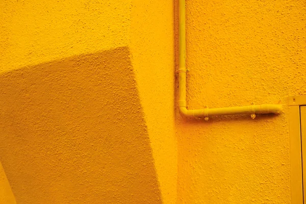 Detail of a gas pipe painted as a house textured wall in yellow in Burano, Italy.