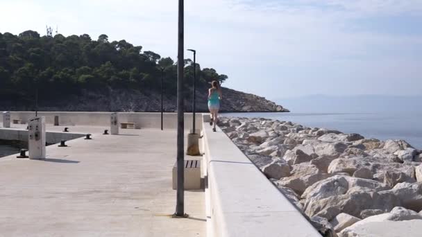 Croacia. Makarska. Una joven corre por el muelle a lo largo de la orilla del mar — Vídeos de Stock