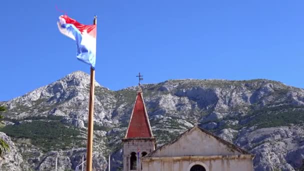 Makarska. Croacia. Vista de la antigua iglesia de la montaña y la bandera en el viento — Vídeo de stock