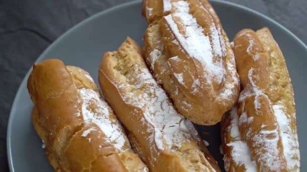 Fresh eclairs sprinkled with powder rotate on the table — Stock Video