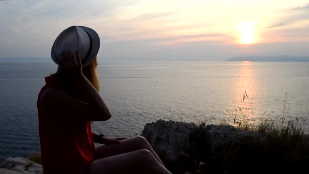 Девушка смотрит на закат над морем, думая о смысле жизни — стоковое видео