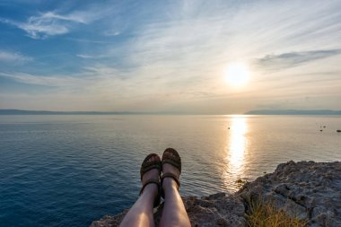 güneşin içinde deniz önünde çim oturan kız