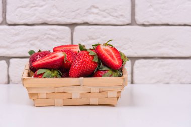 beyaz bir masa üzerinde ahşap bir sepet içinde taze çilek ve bir tuğla duvara karşı