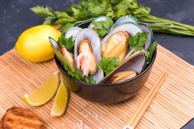 Maydanozlu haşlanmış midye ve siyah tabakta limon.