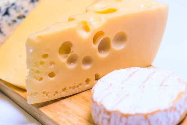 Deliciosos trozos de queso diferente sobre una mesa blanca — Foto de Stock