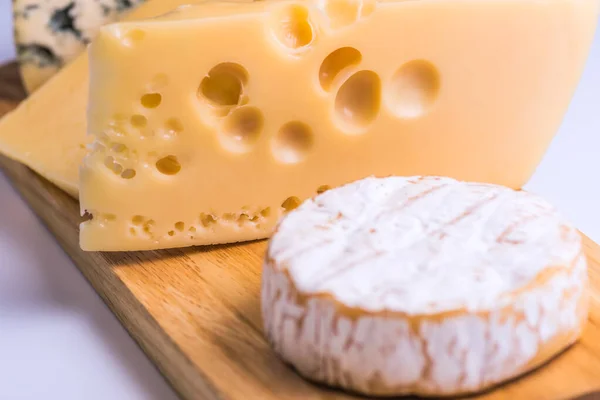Deliciosos trozos de queso diferente sobre una mesa blanca — Foto de Stock
