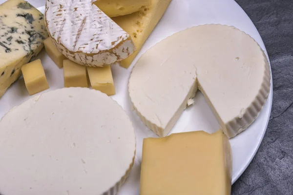 Varios quesos sobre un plato blanco sobre un fondo oscuro — Foto de Stock