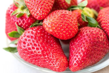 Hafif arka planda çilekli bir tabağın makro fotoğrafı. Taze vejetaryen tatlı