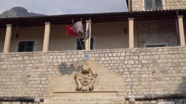 Kotor, Montenegró. A nemzeti montenegrói zászló és a város zászlója a régi város bejárata felett lebeg. — Stock videók