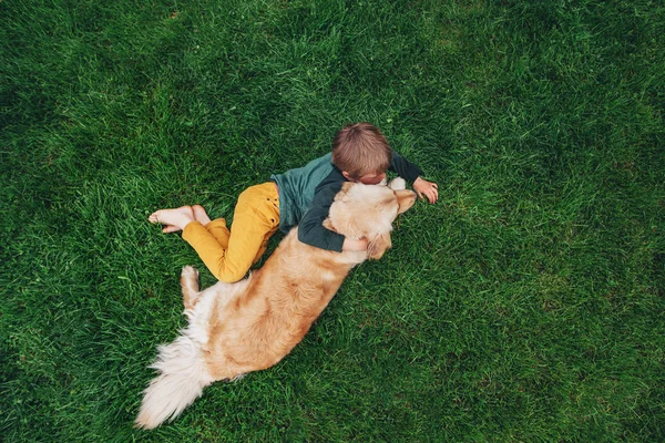 Visão Aérea Menino Deitado Grama Abraçando Seu Cão Golden Retriever — Fotografia de Stock