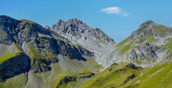 Sersemletici dağ manzarası kayalık zirveler ve canlı yeşil tepeler, parlak güneş ışığı ile aydınlatılmış, doğa harikalarının keşfi ve takdir edilmesi davetkar.