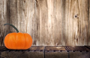 Parlak turuncu balkabağı, ahşap bir masanın üzerinde oturur, kırsal ahşap bir zemin ile çevrili, ılık bir sonbahar atmosferi ve mevsimsel cazibeyi çağrıştırır.