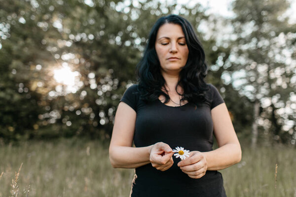 A portrait of a woman counting the petals on a daisy. A woman plucking a petal from a white daisy flower.