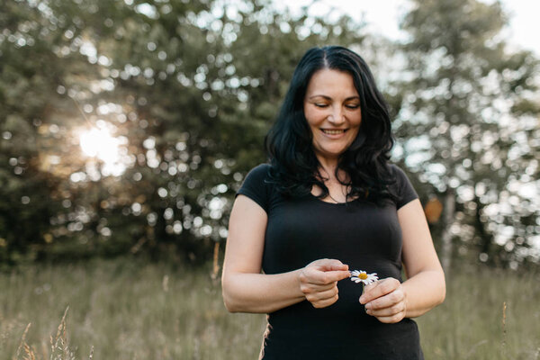 A portrait of a happy woman counting the petals on a daisy. A smiling woman plucking a petal from a white daisy flower.