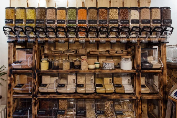 Wooden shelf with refillable food dispensers and containers in package free grocery store. Zero waste shop - rack with glass jars full of dry food in organic shop.